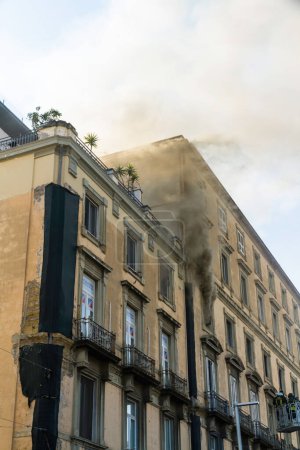 Photo for Naples, Italy - February 15th 2023 - Domestic apartment fire with smoke billowing from window. Garibaldi Square, Naples, Italy. Fire engine basket or cage with two firemen bottom left. - Royalty Free Image