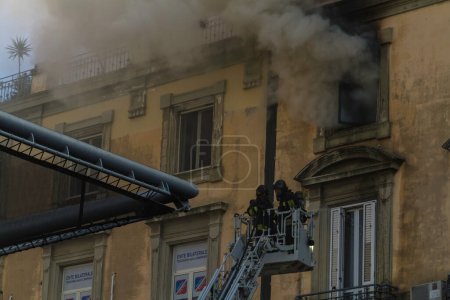 Photo for Naples, Italy - February 15th 2023 - Domestic apartment fire with smoke billowing from window. Garibaldi Square, Naples, Italy. Magirus Fire engine basket or cage with two firemen in breathing apparatus near the fire, landscape - Royalty Free Image