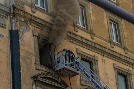 Photo for Naples, Italy - February 15th 2023 - Domestic apartment fire with smoke billowing from window. Garibaldi Square, Naples, Italy. Magirus Fire engine basket or cage with one fireman, landscape, telephoto. - Royalty Free Image