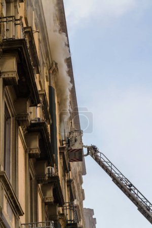 Photo for Naples, Italy - February 15th 2023 - Domestic apartment fire with smoke billowing from window. Garibaldi Square, Naples, Italy. Magirus Fire engine ladder extended with basket or cage, portrait. - Royalty Free Image