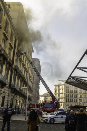Photo for Naples, Italy - February 15th 2023 - Domestic apartment fire with smoke billowing from window. Garibaldi Square, Naples, Italy. Magirus Fire engine ladder extended with basket or cage with one fireman, people at Garibaldi Station, portrait. - Royalty Free Image
