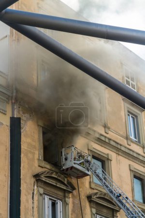 Photo for Naples, Italy - February 15th 2023 - Domestic apartment fire with smoke billowing from window. Garibaldi Square, Naples, Italy. Fire engine basket or cage with one fireman. - Royalty Free Image