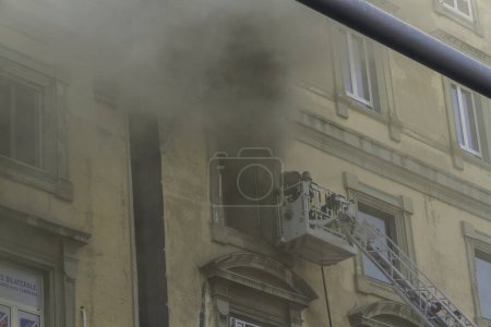Photo for Naples, Italy - February 15th 2023 - Domestic apartment fire with smoke billowing from window. Garibaldi Square, Naples, Italy. Fire engine basket or cage with two firemen, from canopy of Garibaldi Station, telephoto, smoke haze. - Royalty Free Image