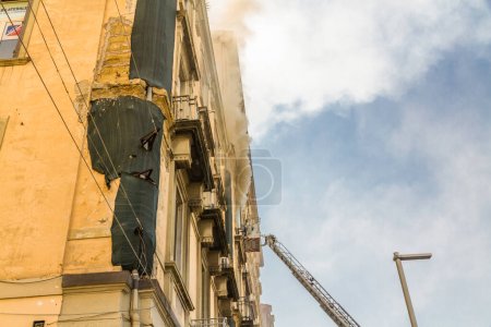 Photo for Naples, Italy - February 15th 2023 - Domestic apartment fire with smoke billowing from window. Garibaldi Square, Naples, Italy. Magirus Fire engine ladder extended with basket or cage, landscape wide angle. - Royalty Free Image