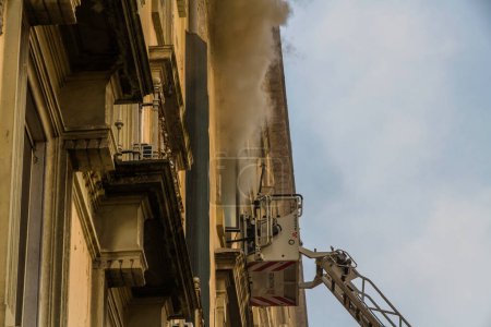 Photo for Naples, Italy - February 15th 2023 - Domestic apartment fire with smoke billowing from window. Garibaldi Square, Naples, Italy. Magirus Fire engine ladder extended with basket or cage, landscape. - Royalty Free Image