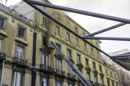 Photo for Naples, Italy - February 15th 2023 - Domestic apartment fire with smoke billowing from window. Garibaldi Square, Naples, Italy. Fire engine basket or cage with one fireman, landscape, wide angle. - Royalty Free Image