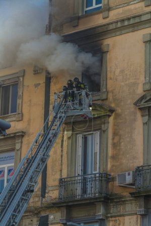 Photo for Naples, Italy - February 15th 2023 - Domestic apartment fire with smoke billowing from window. Garibaldi Square, Naples, Italy. Magirus Fire engine basket or cage with two firemen in breathing apparatus, portrait. - Royalty Free Image