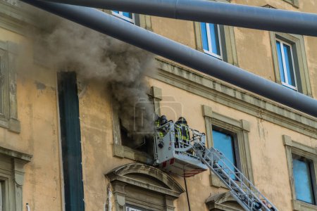 Photo for Naples, Italy - February 15th 2023 - Domestic apartment fire with smoke billowing from window. Garibaldi Square, Naples, Italy. Fire engine basket or cage with two firemen, from canopy of Garibaldi Station landscape, telephoto - Royalty Free Image