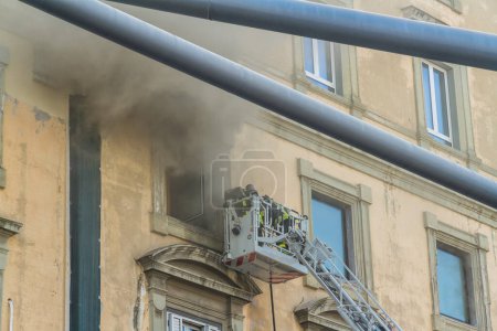 Photo for Naples, Italy - February 15th 2023 - Domestic apartment fire with smoke billowing from window. Garibaldi Square, Naples, Italy. Fire engine basket or cage with two firemen, from canopy of Garibaldi Station, telephoto - Royalty Free Image