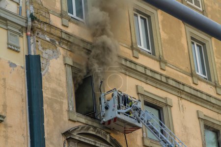 Photo for Naples, Italy - February 15th 2023 - Domestic apartment fire with smoke billowing from window. Garibaldi Square, Naples, Italy. Magirus Fire engine basket or cage with one fireman, landscape. - Royalty Free Image