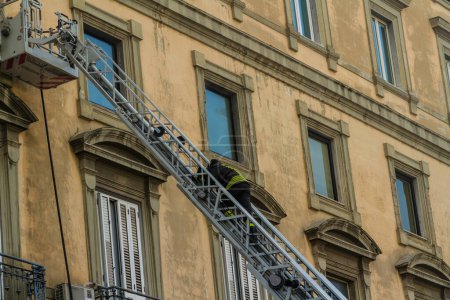 Photo for Naples, Italy - February 15th 2023 - Domestic apartment fire with smoke billowing from window. Garibaldi Square, Naples, Italy. Magirus Fire engine basket or cage with fireman climbing on ladder, landscape. - Royalty Free Image