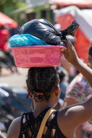 Photo for Scenes from the Haitian market near the border with Haiti. Haitian Woman carrying a plastic bucket willed with goods on her head shot from behind. - Royalty Free Image
