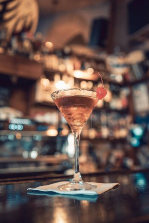 Warm, cozy bar interiors. Close up shot of a beautiful brown liqueur or drink in a martini glass, with a sweet red candied cherry on the edge of the glass. Adult relax.