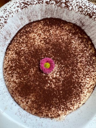 Nahaufnahme von oben eines modernen Restaurant-Tiramisu-Desserts mit essbarer Blumendekoration.