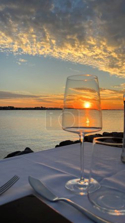 Foto de Sun is going down inside a glass of wine in a luxury seaside restaurant. Magic moments while fine dining. - Imagen libre de derechos
