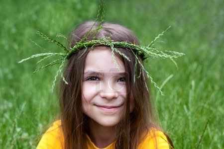 Foto de Una niña pequeña en una corona de espiguillas de hierba sobre un fondo de vegetación borrosa. Antigua fiesta eslava de Ivan Kupala - Imagen libre de derechos
