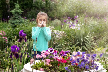 Photo for Allergy. A girl covers her nose with a napkin from an allergic reaction to blooming flowers near a flower bed. Allergy concept. Copyspace. - Royalty Free Image