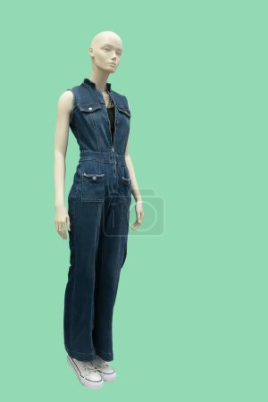 Full length image of a female display mannequin wearing blue denim jumpsuit isolated on green background