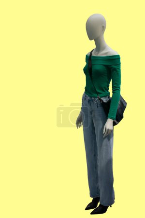 Ganzes Bild einer weiblichen Schaufensterpuppe in grüner Strickbluse und blauer Jeans auf gelbem Hintergrund