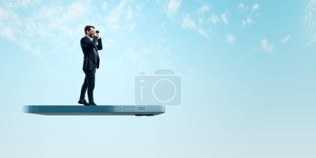 Eine Miniaturfigur eines Mannes im Anzug steht auf einem riesigen Smartphone und blickt mit Ferngläsern in die Ferne vor einem klaren blauen Himmel, der Vision und Chance darstellt.