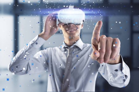 Attractive young european man pointing at abstract hologram with VR glasses in blurry office interior. Augmented reality and cyberspace concept