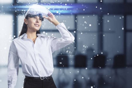 Attractive young european businesswoman with abstract hologram and VR glasses in blurry office interior. Augmented reality and cyberspace concept