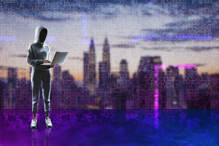 Hacker in hoodie holding laptop and standing on abstract glowing pixel wall blurry city background. Large led projection screens and data hacking concept