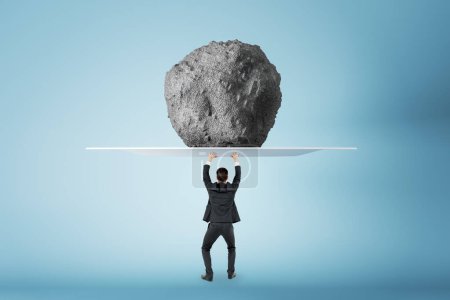 Photo for Success, power and strength concept with businessman back view holding huge stone. above his head, feeling tired on blue background - Royalty Free Image