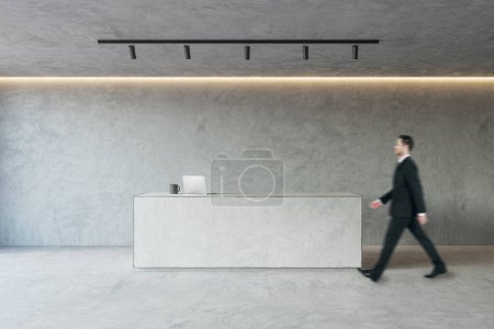 Side view of young businessman walking in modern concrete office reception interior with desk. Lobby concept. Worker and CEO concept