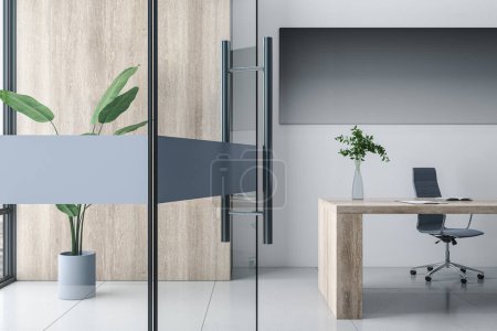 Bright concrete, glass door and wooden stylish designer office interior with furniture, supplies, laptop, decorative plant and mock up poster on wall. 3D Rendering.