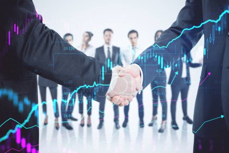 Close up of two males shaking hands with their diverse blurry colleagues in the background. Concept of business partnership, management and financial growth with forex chart. Double exposure