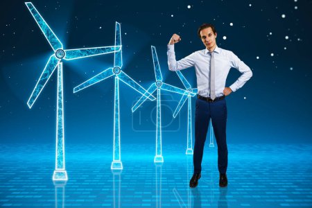 Photo for Young businessman flexing muscle and looking at glowing digital wind mill turbine hologram on blue background. Wind generator concept - Royalty Free Image
