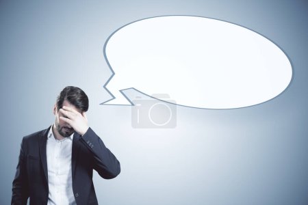 Photo for Anxious young businessman with empty speech bubble on gray background. Opinion and mock up place - Royalty Free Image