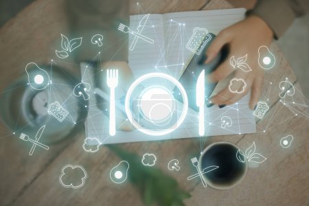 Photo for Futuristic restaurant menu application concept with glowing silverware hologram on blurry background. Top view of hands using cellphone on blurry desktop background with copybook, coffee cup and other items. Double exposure - Royalty Free Image