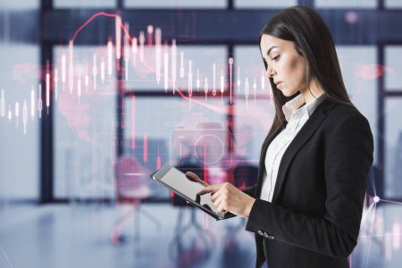 Attractive young european businesswoman using digital pad with glowing falling red forex chart on blurry office interior background. Stock exchange and crisis concept. Double exposure