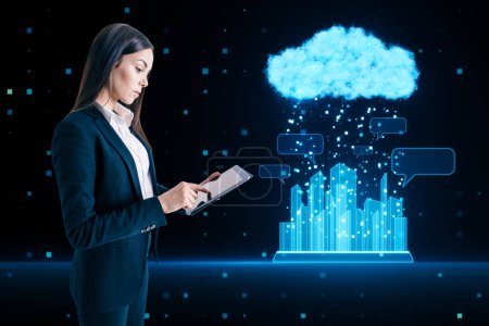Attractive young european businesswoman using tablet with glowing urban cloud and city communication hologram on blurry blue tech background. Smart city and IOT concept