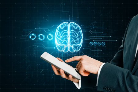 Großaufnahme einer männlichen Hand, die auf ein Mobiltelefon zeigt, mit leuchtendem Gehirn-Hologramm auf verschwommenem dunklen Schaltkreis-Hintergrund. Künstliche Intelligenz und maschinelles Lernkonzept