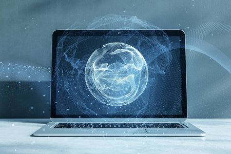 Close up of laptop on desktop with polygonal globe hologram on blurry background. World map with global social network. Future concept. Blue futuristic background with planet. Double exposure