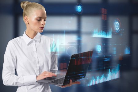 Photo for Attractive blonde businesswoman using laptop with glowing digital business interface with charts on blurry office interior background. Infographic and big data concept. Double exposure - Royalty Free Image