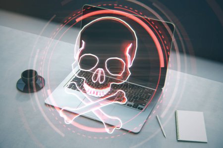 Close up of laptop, notepad and coffee cup on desktop with digital red skull on blurry background. Ransomeware, virus and pirate threat concept. Double exposure