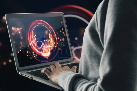 Hacker benutzen Laptop mit digitalem Totenkopf-Hologramm auf dunklem Hintergrund. Ransomeware, Viren- und Piratenbedrohungskonzept. Doppelbelastung