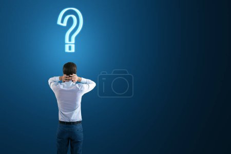 Photo for Back view to a thoughtful businessman and a question mark on his head on a dark blue background with empty space, search for a solution and doubt concept, mockup - Royalty Free Image