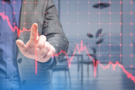 Close up of businessman hand pointing at falling red business graph grid on blurry office interior background. Crisis, recession and stock market concept. Double exposure