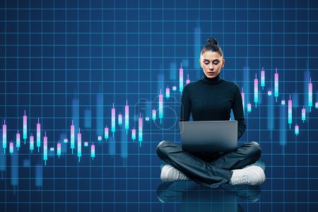 Thoughtful young european woman sitting on floor using laptop with creative growing candlestick forex chart on blue grid background. Financial growth and stock concept