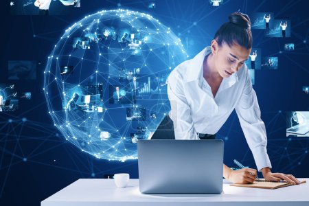 Geschäftsleute vernetzen, Videokonferenzkonzept. Attraktive europäische Frau lehnt am Schreibtisch mit Laptop und schreibt mit abstrakten blauen Globus mit polygonalem Netz und Bildern auf verschwommenem Hintergrund