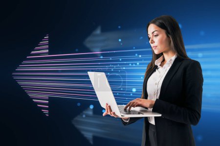 Photo for Side view of attractive young european businesswoman using laptop with glowing digital arrow made up of blue tech lines on dark background. Market, technology and top concept - Royalty Free Image
