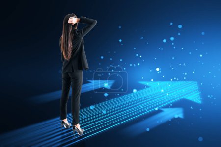 Back view of thoughtful young european businesswoman with glowing digital arrow made up of blue tech lines on dark background. Market, technology and top concept