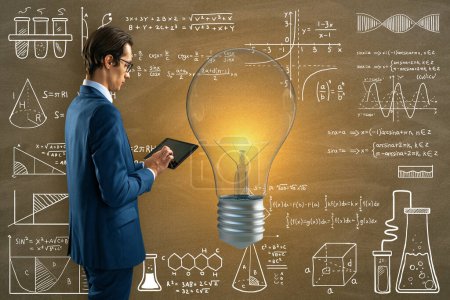 Attrayant réfléchi jeune homme d'affaires européen utilisant une tablette avec ampoule lumineuse sur fond de mur de tableau noir avec des formules mathématiques. Science, idées et éducation