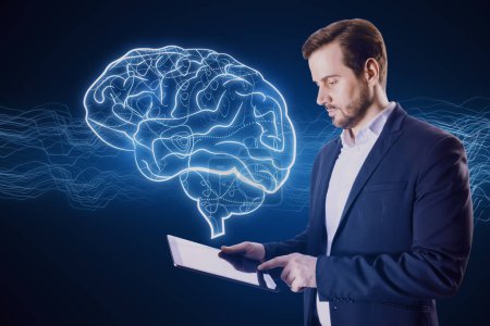Portrait of attractive young businessman with tablet and creative digital brain hologram on blue background. Hi-tech innovation and AI concept