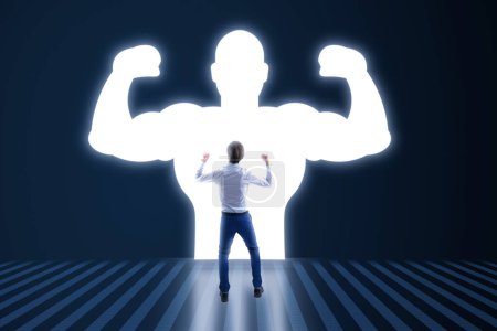 Back view of young businessman with very strong illuminated shadow flexing muscles on dark wall background. Personal development, inner strength, motivation concept